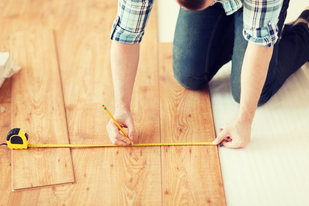 Male hands measuring wood flooring - Deerfoot Carpet & Flooring